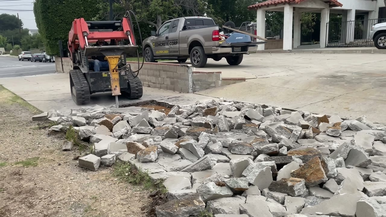 Track loader with a breaker removing an old concrete slab, Level Line truck behind