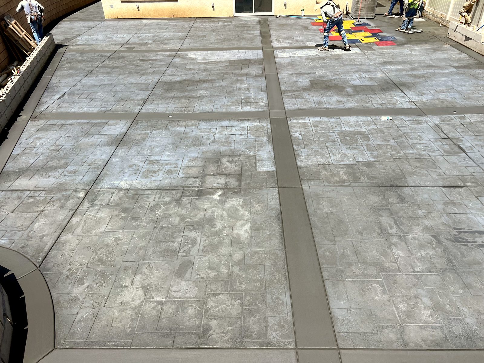 Crew stamping a large backyard patio with slate-pattern texture mats
