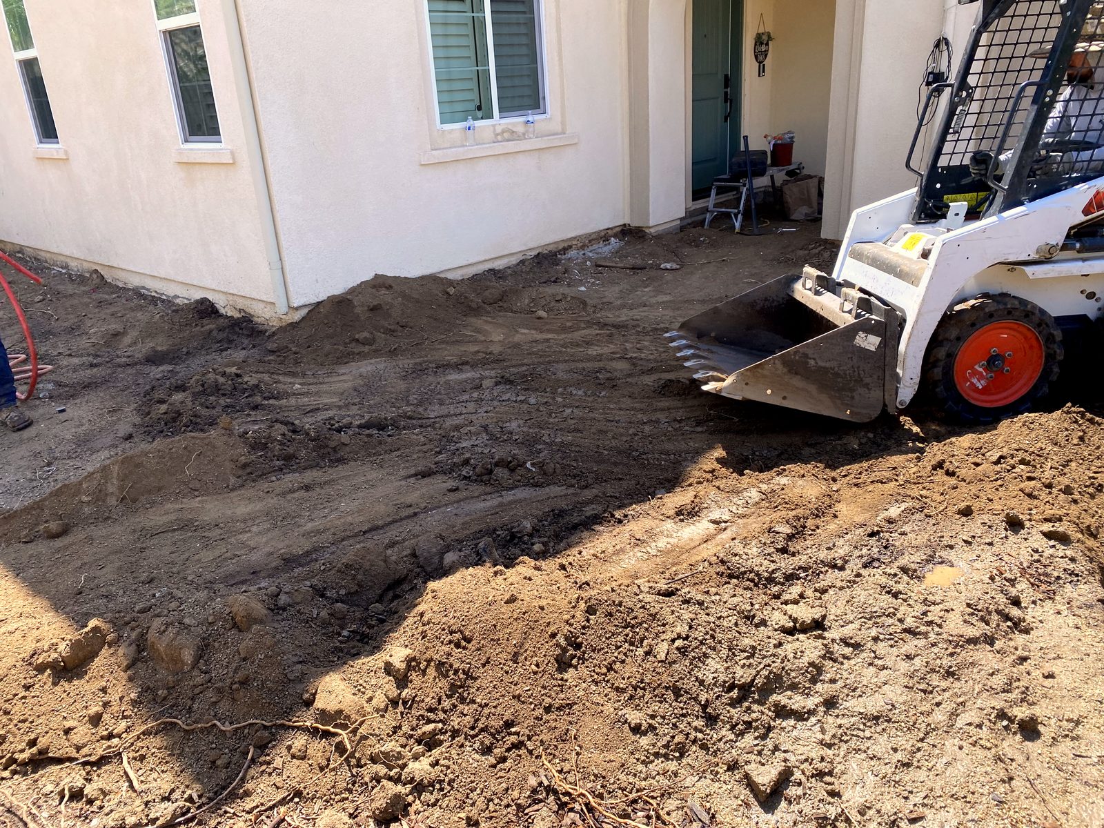 Level Line crew grading and compacting the base of a backyard with a skid-steer before any concrete is placed
