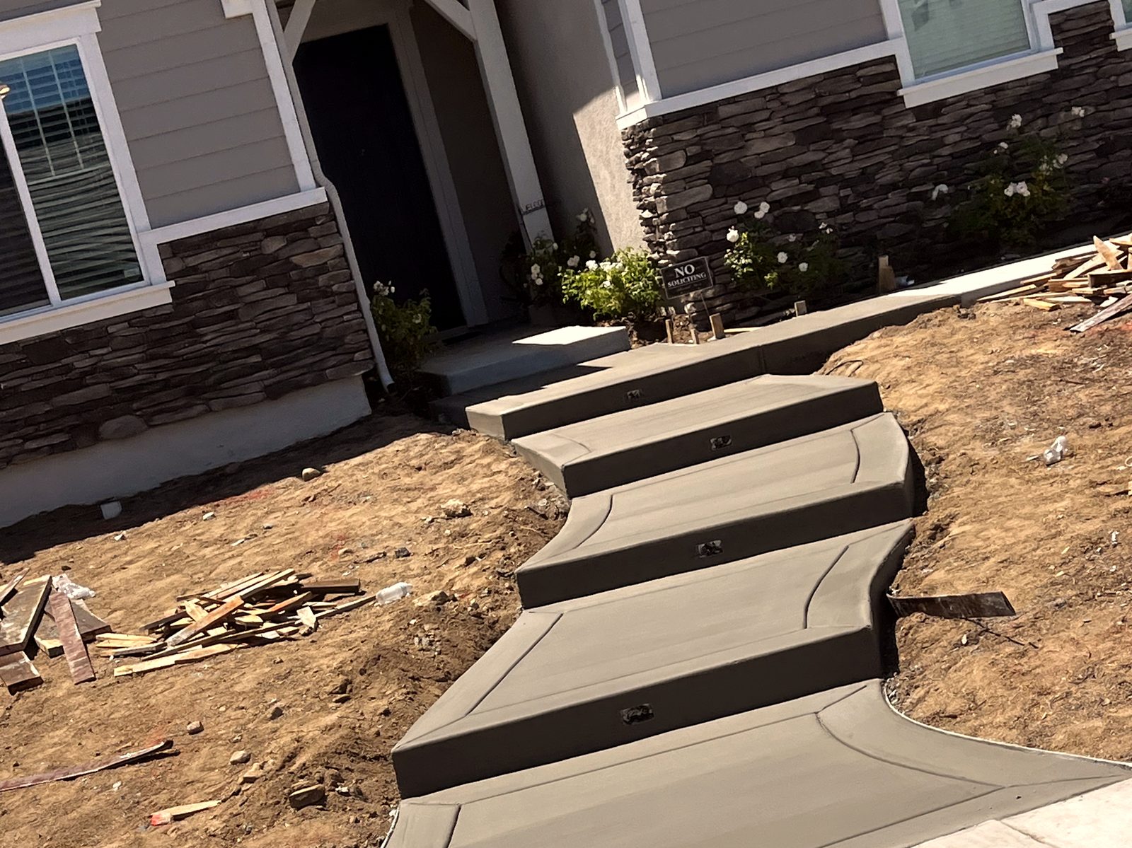 Freshly poured concrete walkway and floating steps leading to a new home's front door