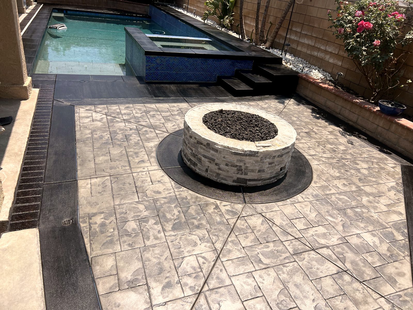 Stamped concrete pool deck with a stone fire pit beside a backyard pool and spa